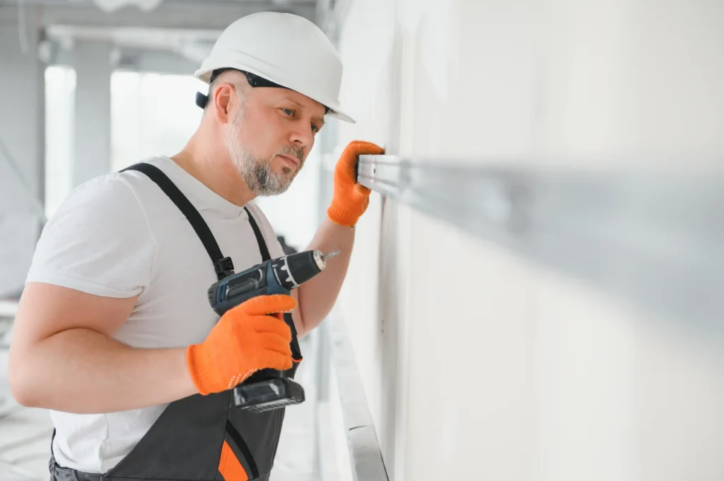 Construction worker using a power drill to install drywall in Edmonton home renovation project