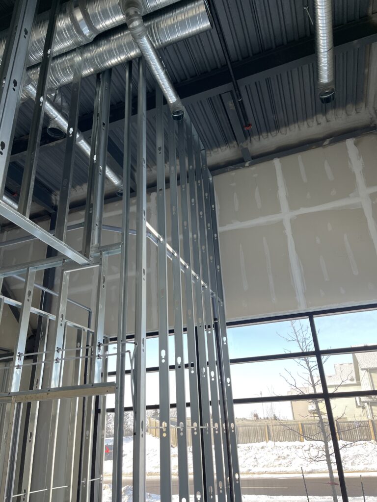 Commercial interior with metal stud framing and drywall seams taped and mudded near a large window